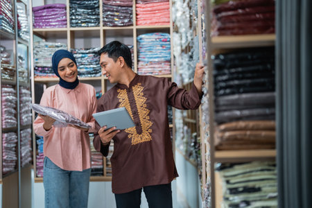 male and muslim Female worker checking product quality and stock at fashion shop warehouse holding tabletの写真素材