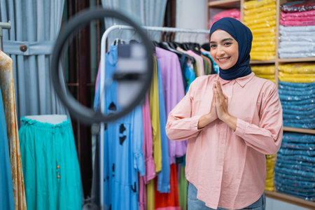 attractive muslim woman reviewing fashion product and doing live selling session on social media from her shopの写真素材