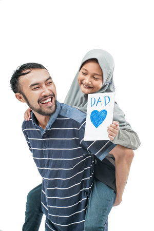 portrait of happy dad giving a piggyback ride with muslim daughter holding a love card for fathers dayの写真素材