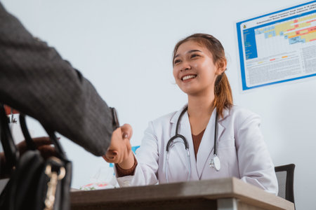 a female doctor in doctors coat with long brown hair smiling while hand shake with the patientの写真素材