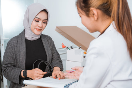 a beautiful patient with grey veil pointing on the paper in front of the female doctor with long brown hairの写真素材