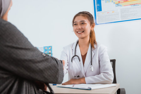 a beautiful doctor in doctors coat smiling while hand shake with the female patient with grey veilの写真素材