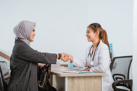 a female patient with grey veil and grey cardigan hand shake with the beautiful doctor in doctors coatの写真素材