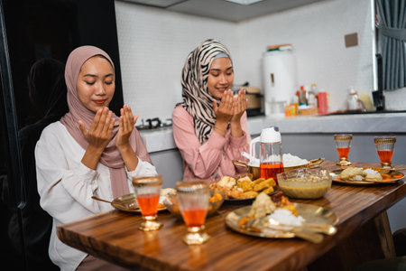 two woman pray before meals when breaking the fast together at homeの写真素材