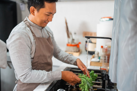 young man is preparing dinner at home by himself. wash the vegetable in the sinkの写真素材
