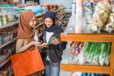 Two Muslim girls smiling while holding the packaging of a product in a supermarketの写真素材