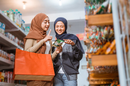 Two Muslim girls in masks observing items while shopping together in a storeの写真素材