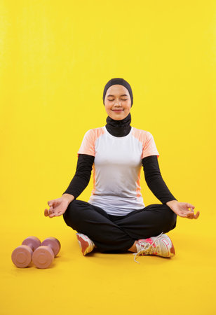 Muslim woman in sportswear sit and close eyes during yoga on yellow backgroundの写真素材