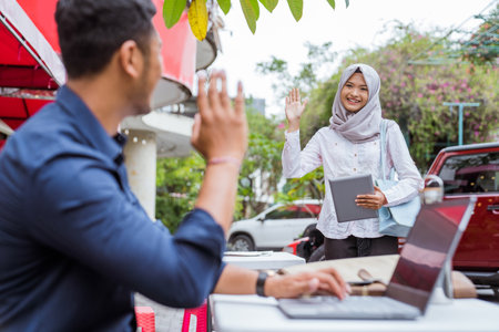asian woman in veil comes with tablet waving when meeting male friend at coffee shopの写真素材