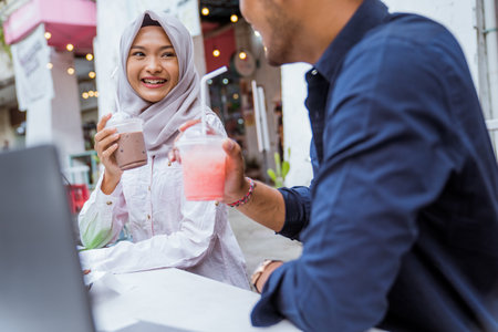 attractive veiled woman sits jokingly enjoying drinks during iftar with boyfriend at coffee shopの写真素材