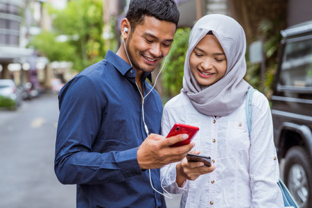 Asian men and women in veil chatting and using cellphones together outdoorsの写真素材