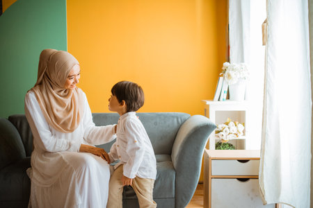 Asian Muslim mom chats with little boy sitting on the sofa in the living roomの写真素材