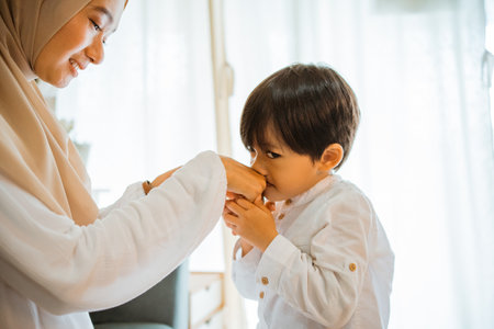 asian little boy kissing moms hand during Eid celebration at homeの写真素材