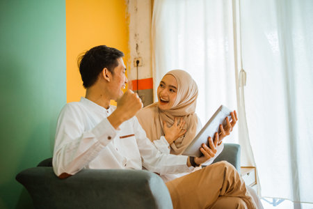 portrait of excited Asian couple sitting on couch while using digital tablet at homeの写真素材