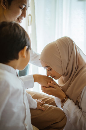 Asian Muslim mother kissing fathers hand with son during Eid celebration as form of obedienceの写真素材