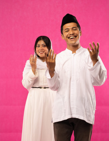 portrait of happy Asian Muslim couple stand with praying hand gesture on pink background