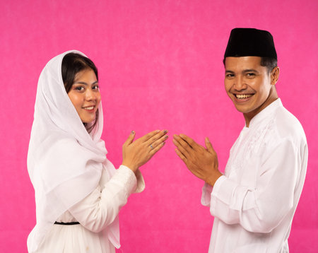 close up of happy Asian couple with greeting gesture in moslem clothes on pink background