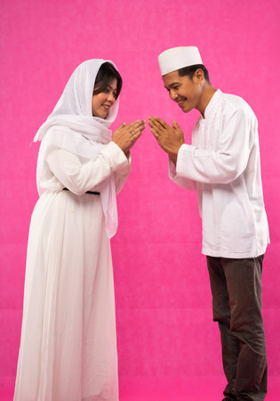 side view of Asian couple with greeting gesture in moslem clothes with pink background