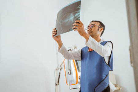 a male vet in x-ray protective apron observing the x-ray result against the x-ray machine at the...
