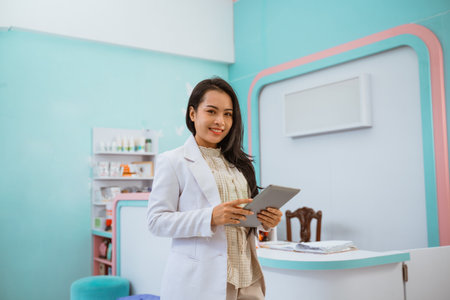 Female vet standing in front of the receptionist desk with tablet on her hand and smiling.の写真素材