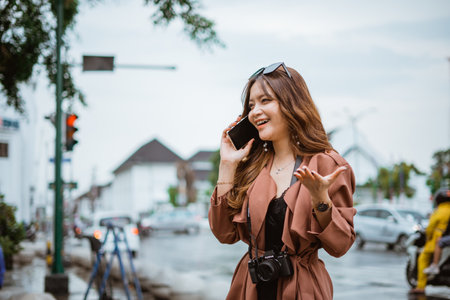 female traveller raising her hand while calling on phone at the sidewalkの写真素材
