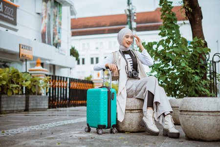 female traveller with hijab touch her head while sitting on the stone seat and leaning her hand on...