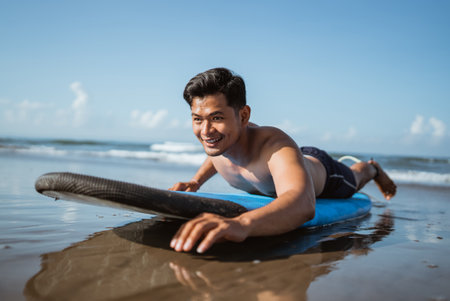 handsome young male surfer rowing on a surfboard while practicing on the sand at the beachの写真素材