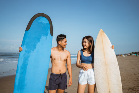 portrait of happiness asian young couple while chatting holding surfboards at the beachの写真素材