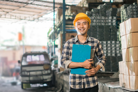 asian man factory employee wearing helmet standing with clipboard in factoryの写真素材