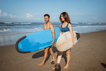 summer travel vacation happy couple friends walking along the beach carrying surfboardsの写真素材