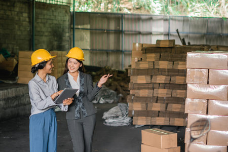two Asian female factory workers stand near goods in a warehouse