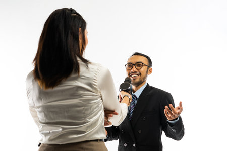 a female journalist with long brown hair standing interviewing an adult men in black suit using a black microphoneの写真素材