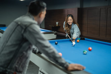 female pool player poking the white ball while the male player standing at the side of the pool