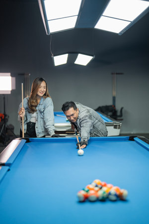 male pool player with glove while poking the white ball with the female player standing beside him