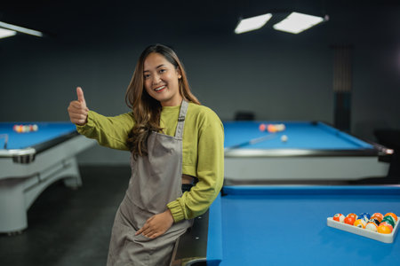 beautiful bar worker smiling while standing showing thumb up on the pool at the billiard studioの写真素材