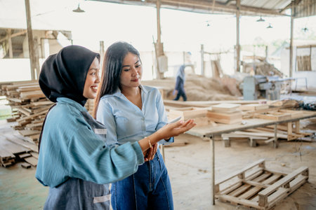 female Muslim entrepreneur serving female customers viewing and choosing at wood craft workshopの写真素材