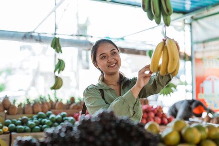 beautiful customer picking the bananas from the hanger at the fruit shopの写真素材
