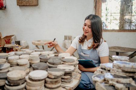 beautiful Asian woman stone craft entrepreneur pointing to a pile of craft stone pieces in a warehouseの写真素材