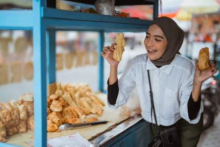 a beautiful girl wearing a hijab sells various kinds of fried food with a cart on the side of the roadの写真素材