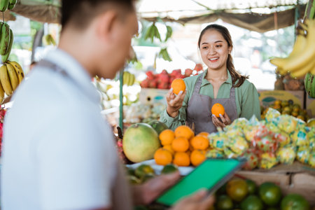 female fruit seller checking the sunkist while the male seller using the digital tabletの写真素材