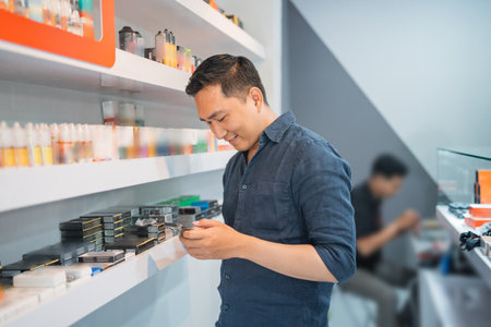 male vape seller looking at his phone while standing beside the store shelfの写真素材