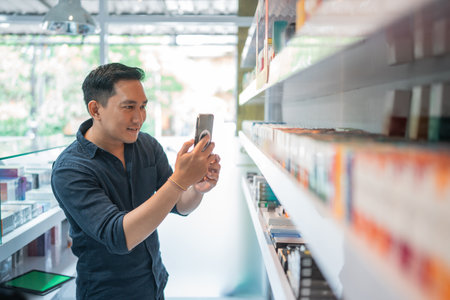 male shopkeeper taking photo of the liquid stock at the shelf using the phoneの写真素材