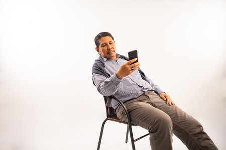asian old man sitting on a chair and using phone for messaging in social media white background isolatedの写真素材