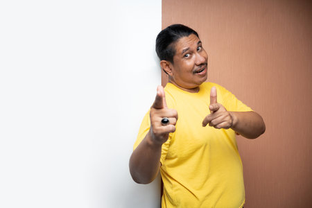 old asian man standing beside empty whiteboard with pointing gesture and looking at camera in plain background isolatedの写真素材