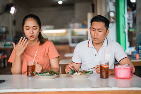 Asian woman and man sitting with a spicy expression while eating pecel in a traditional food stallの写真素材