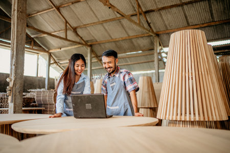 Asian business couple using a laptop computer together at a woodcraft shopの写真素材