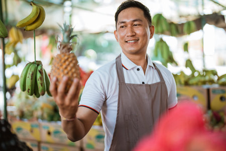 handsome fruit seller smiling while looking at the pineapple at his handの写真素材