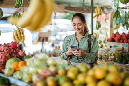 female customer using the phone while standing at the fruit shopの写真素材