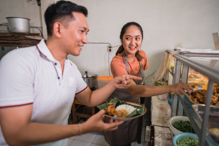 male customer choosing food with pointing finger with a female waitress at a traditional stallの写真素材
