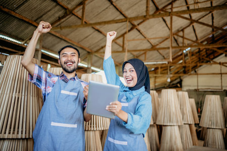 excited entrepreneur couple raises their hands when using a tablet while working at the woodcraft shopの写真素材